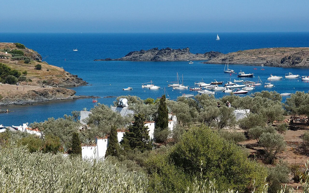 Olive terraces and cypresses running down to the bay of Portlligat with boats in the water