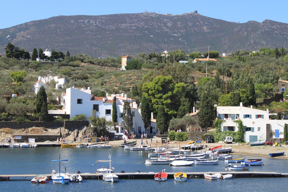 Salvador Dalí's whitewashed house at Portlligat, with white eggs on its roofline, above a cove of moored fishing boats and the Cap de Creus hills